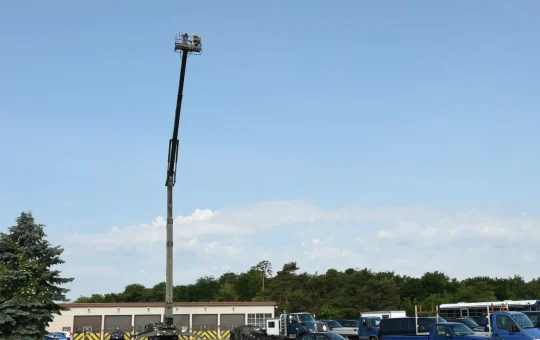 A telescoping boom lift fully extended high against the sky above a parking lot