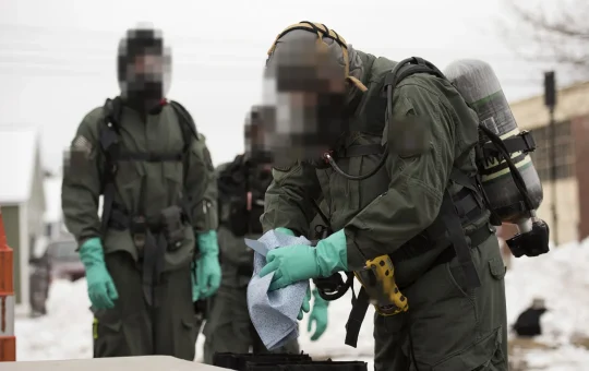 A worker in a chemical suit wipes a gloved hand during decontamination