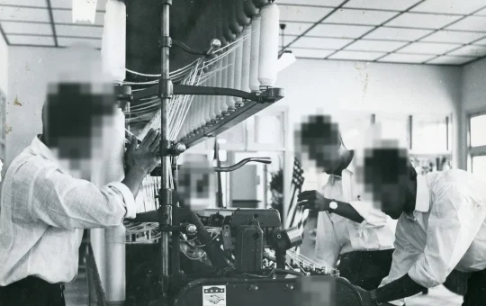 Students tend a roving frame full of bobbins in a textile spinning plant (historical black-and-white photo)