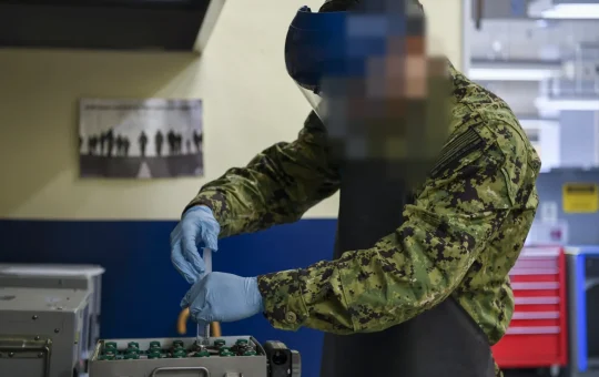 A technician in a face shield, apron and gloves services the cells of a nickel-cadmium battery