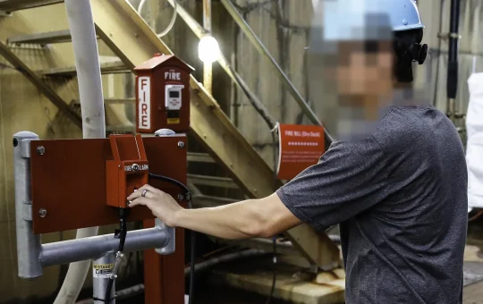 A shipyard worker tests a manual pull station in a dry dock