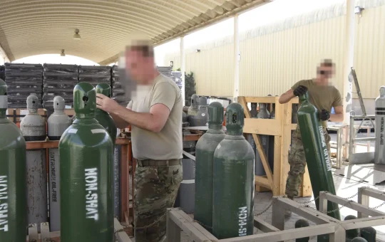 Workers handle green gas cylinders stored upright in a rack