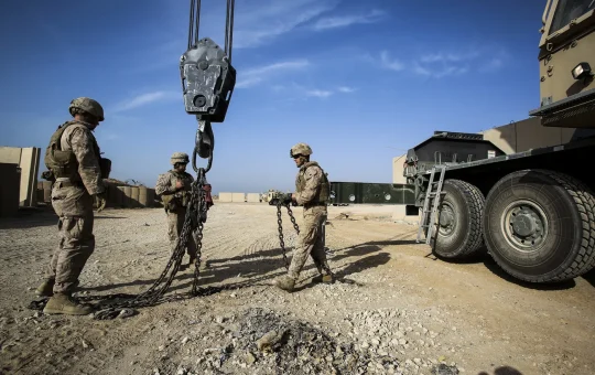 A crane hook block hangs from the boom while two crew stand on the ground below