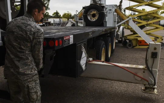 A worker, seen from behind, extends a crane outrigger onto its pad