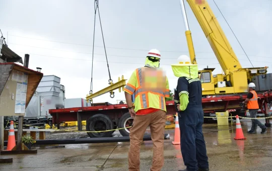 A mobile crane lifts at an electrical substation with overhead power lines behind the boom