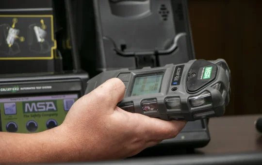A hand holding a portable gas detector beside its test station