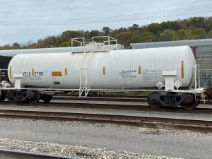 A white hazardous materials tank car standing in a railyard