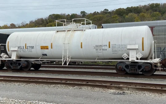 A white hazardous materials tank car standing in a railyard