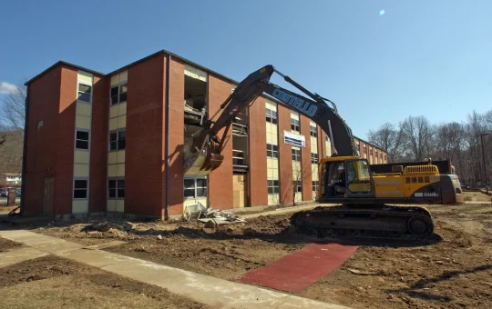 An excavator tears into the corner of a three-story brick building
