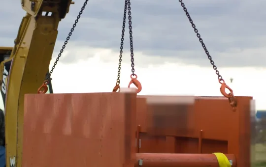 A backhoe lowers a steel trench box into a trench