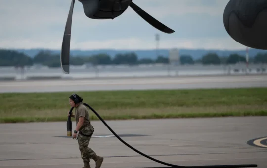A worker carries a heavy power cord across an open ramp