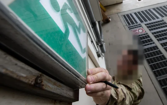 A fire inspector reaches up to check a lighted exit sign mounted over a doorway