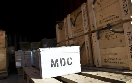 A data card sits on a pallet of stacked explosives crates