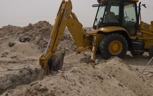 A backhoe digs a trench in sandy ground