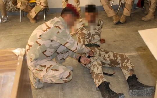 One soldier practices putting a tourniquet on another during a first aid class