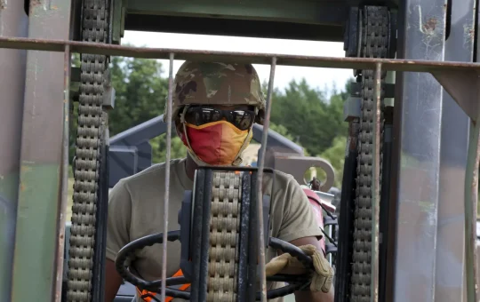 A forklift operator at the wheel, seen through the mast of the truck