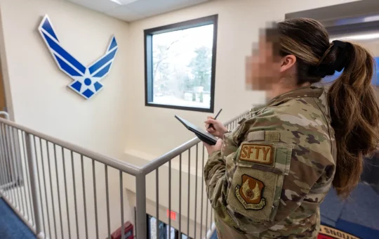 An Air Force occupational safety NCO with a SFTY patch takes notes on a tablet during a facility safety inspection