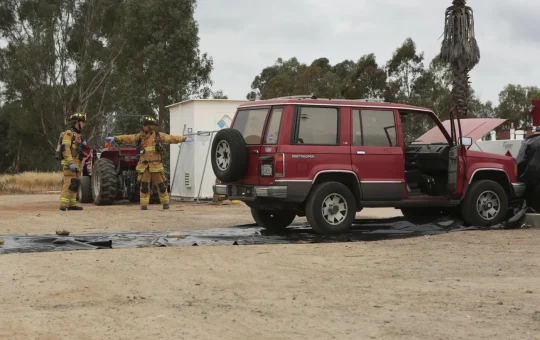 Firefighters survey a simulated spill around a vehicle parked on a containment tarp