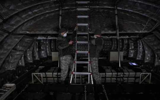 Two workers set up a portable stepladder inside an aircraft cargo bay