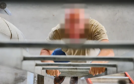 A worker climbs a ladder facing it with both hands on the rungs