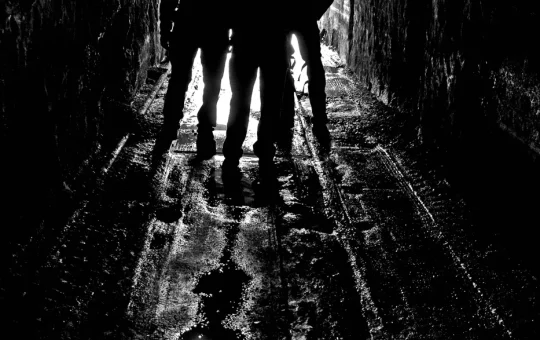 Three miners with cap lamps, in silhouette, walk through an underground mine passage