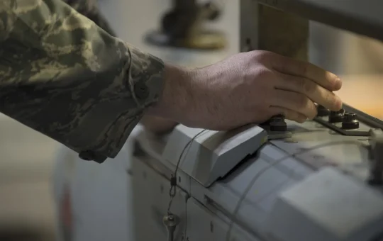 A hand presses the buttons on a gantry crane pendant control