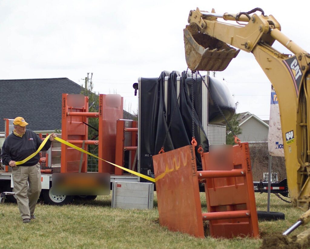 OSHA competent person guiding a trench box into a trench on a construction site