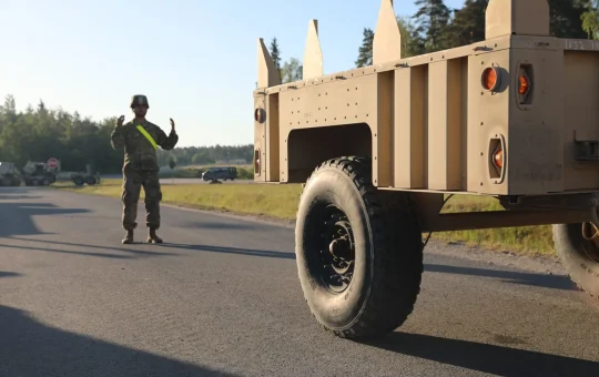 A ground guide stands behind a trailer and signals as it backs up