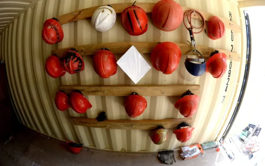 Rows of hard hats hanging on a wooden rack inside a storage container