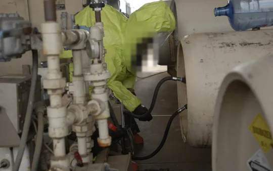 A responder in an encapsulating suit checks the valves on chlorine ton containers in a leak drill