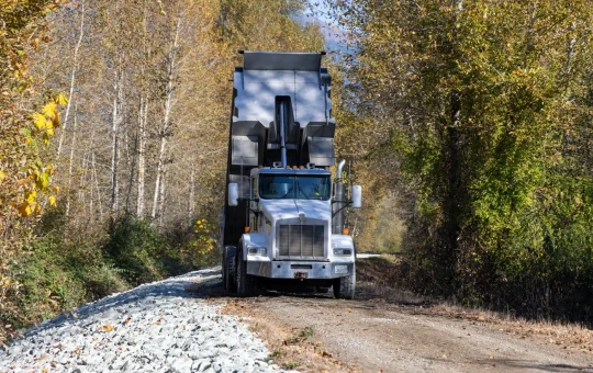 A large dump truck comes head-on down a narrow gravel haul road
