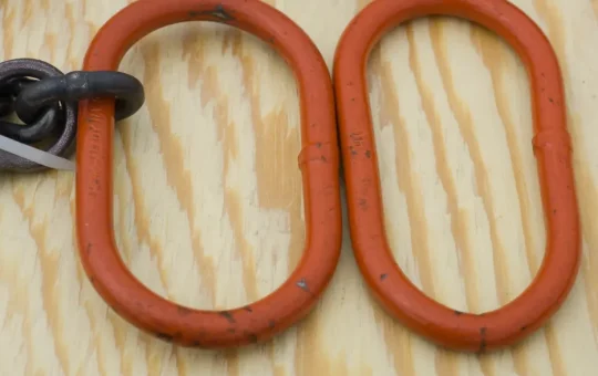 Two orange chain sling master links side by side, the right one bent out of shape