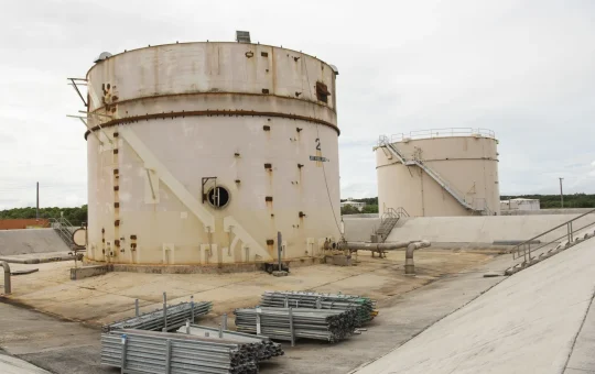 Two large fuel tanks stand inside a walled concrete containment area