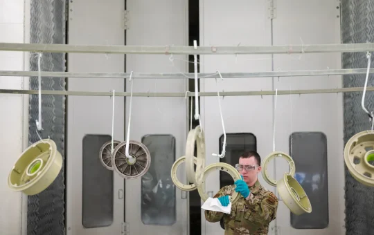 Parts hang from hooks inside a lit paint booth