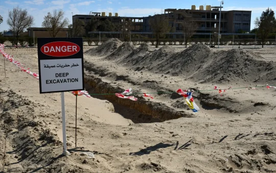 A red danger sign reading deep excavation stands beside a trench on a construction site