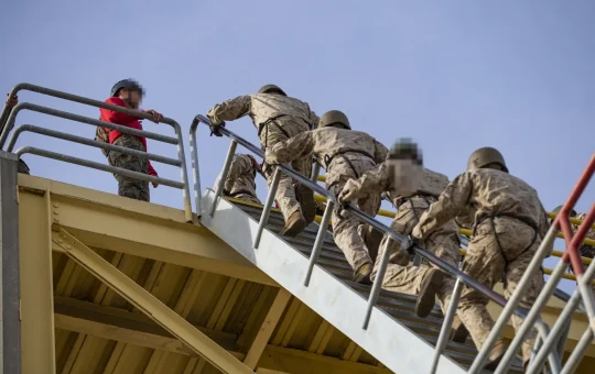 A line of people climbs steep steel stairs holding the handrails
