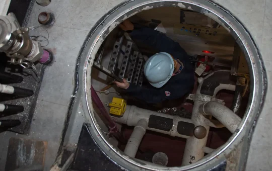 A ladder leads down through a manhole into a void space on a ship