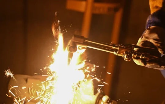 Gloved hands cutting metal with an oxy-acetylene torch, sparks flying